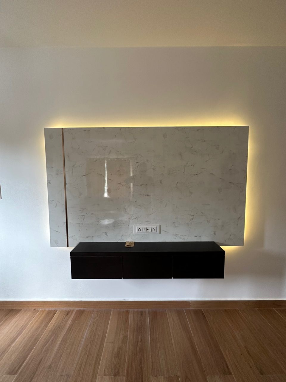 Marble-finish TV feature panel with warm concealed backlighting above a black floating console