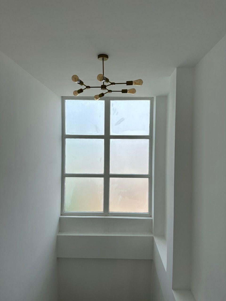 Bright double-height stairwell with a six-pane window, deep sill and a brass multi-arm pendant light