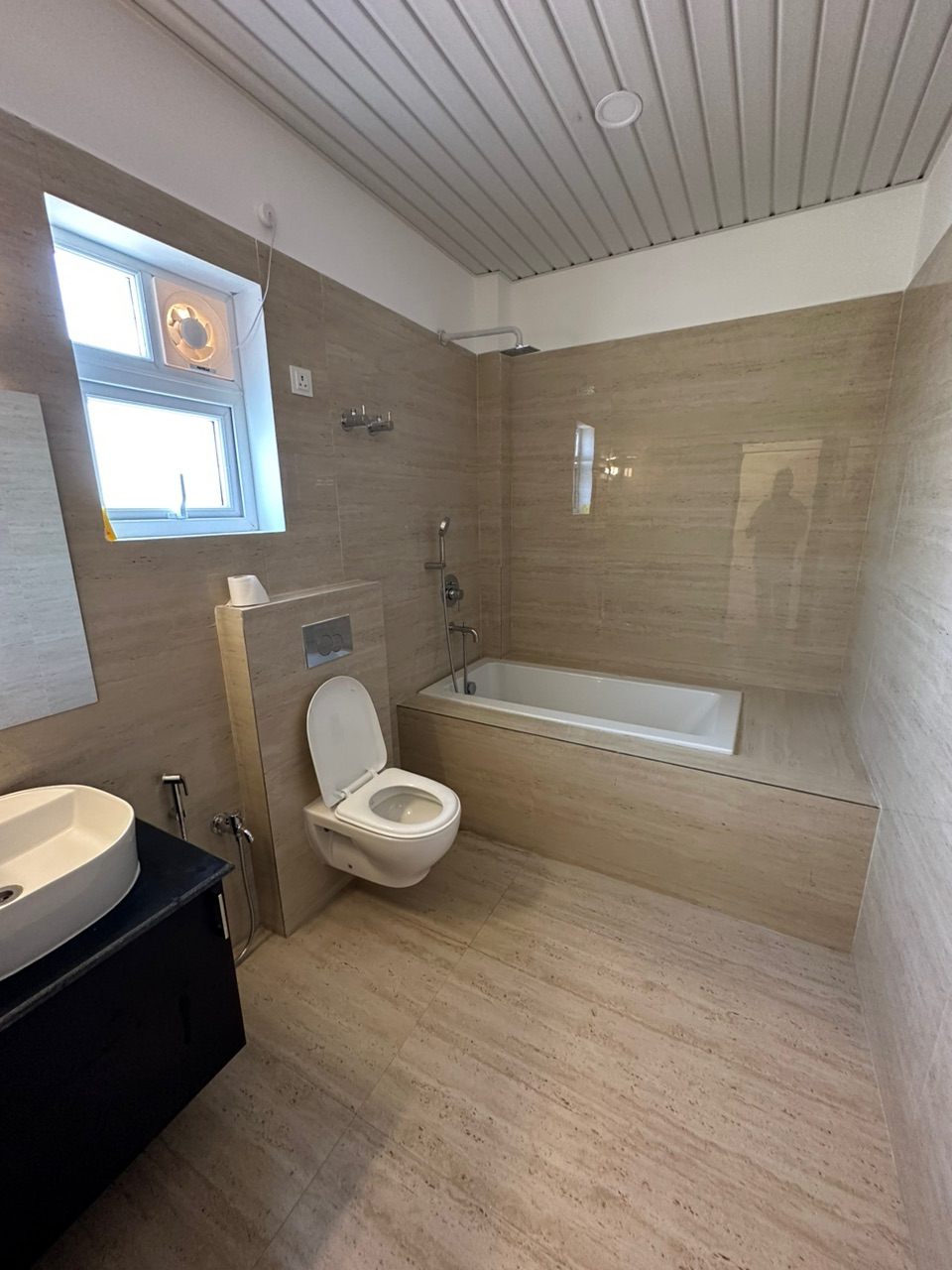 Completed bathroom with travertine-look tiling, a built-in bathtub, wall-hung WC and slatted false ceiling