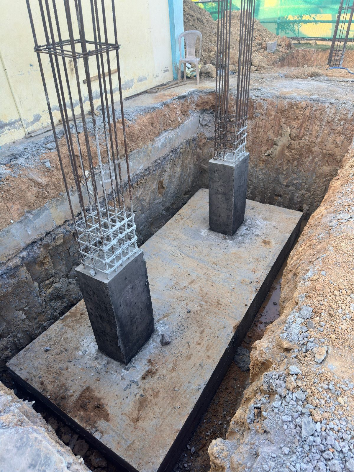 Excavated foundation pit with a concrete raft, two cast pedestals and column reinforcement cages rising from them