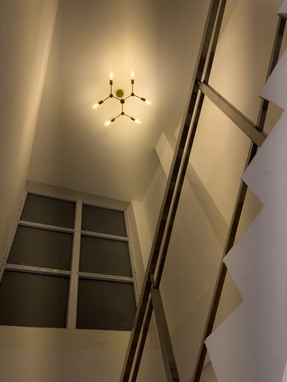 Upward view of a stairwell showing a brass wall light and a polished stainless steel railing against white walls